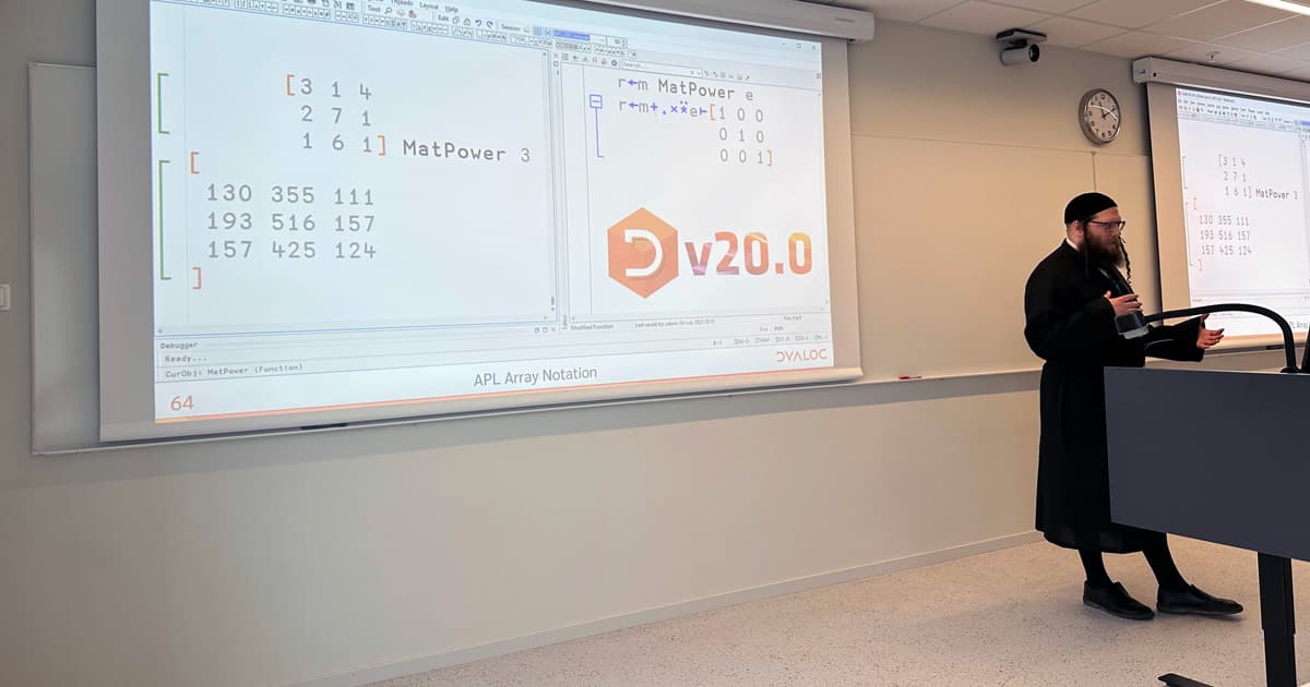 Adám Brudzewsky presenting at PLSS 2025 in Bergen, Norway. He stands at a lectern in front of a projection screen showing APL code and the Dyalog version 20.0 logo, with the topic "APL Array Notation".