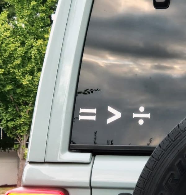 A sticker on the back window of a car that reads "=>÷"